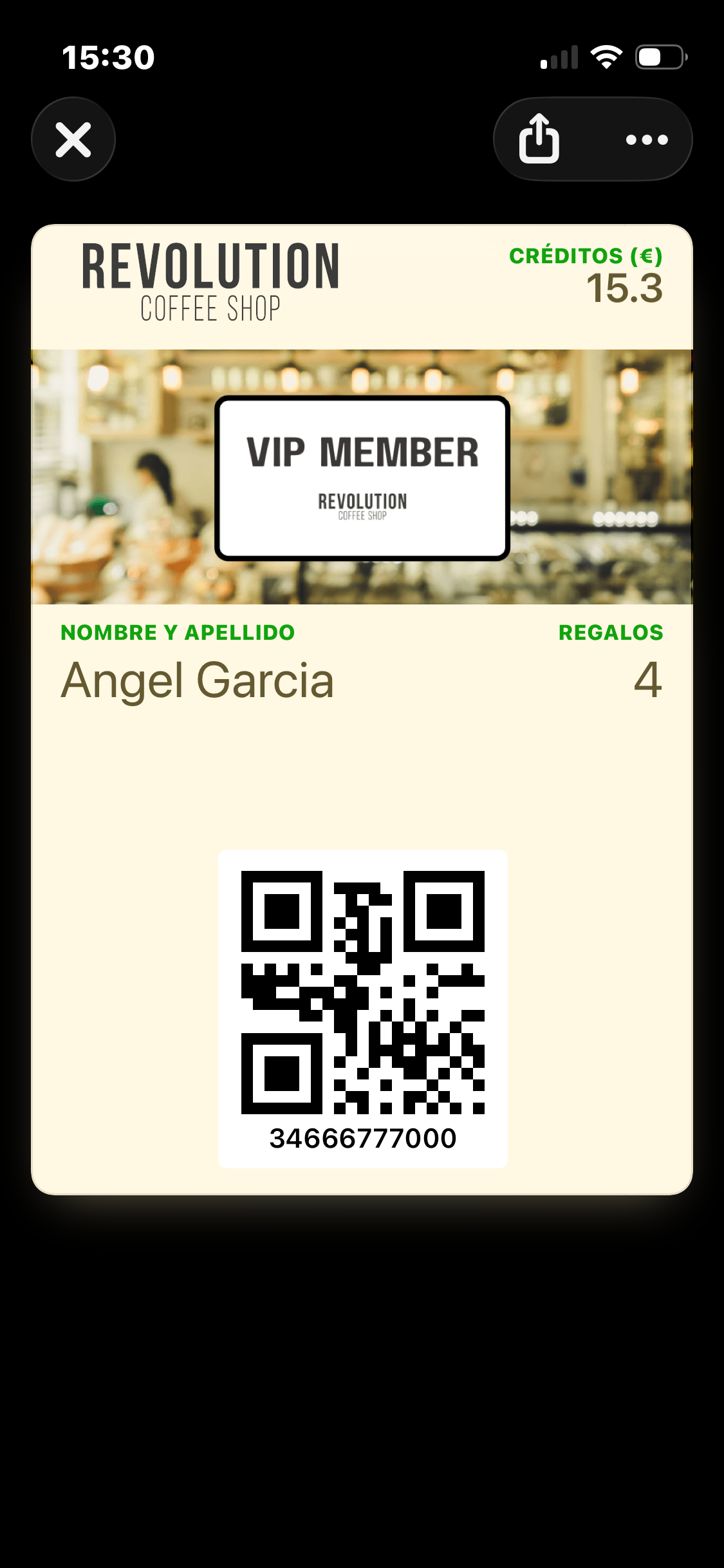 Der Wallet Pass mit bedingter Ansicht auf dem iPhone für ein Mitglied mit dem Tag Nivel_VIP — cremefarbene Karte mit dem Revolution Coffee Shop-Schriftzug oben links, Créditos (€) 15.3 oben rechts, einem VIP MEMBER-Strip-Bild, grünen Beschriftungsfarben und dunkelbraunem Text, Mitglieds-QR und ID am unteren Rand. Dieselben Daten wie der Standard-Pass, nur eine andere visuelle Gestaltung