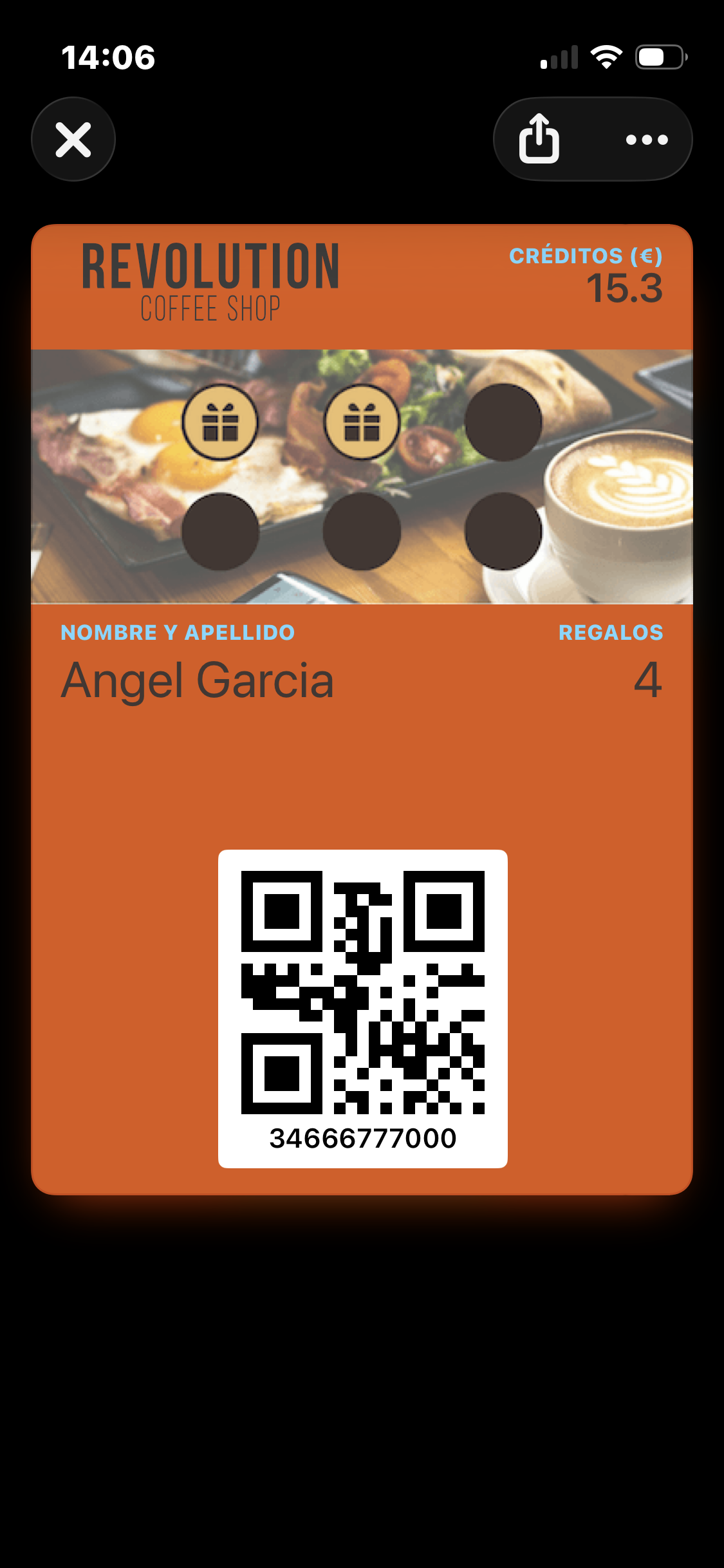Der Wallet Pass auf einem iPhone geöffnet — orangefarbene Karte mit einem Marken-Schriftzug oben links, "Créditos (€) 15.3" oben rechts, ein Frühstücks-Bannerbild mit zwei verdienten Stempeln (Geschenksymbole) und drei nicht verdienten (leere Kreise), Mitgliedsname und Geschenkanzahl über einem Mitglieds-QR-Code, und die Telefonnummer des Mitglieds unter dem QR