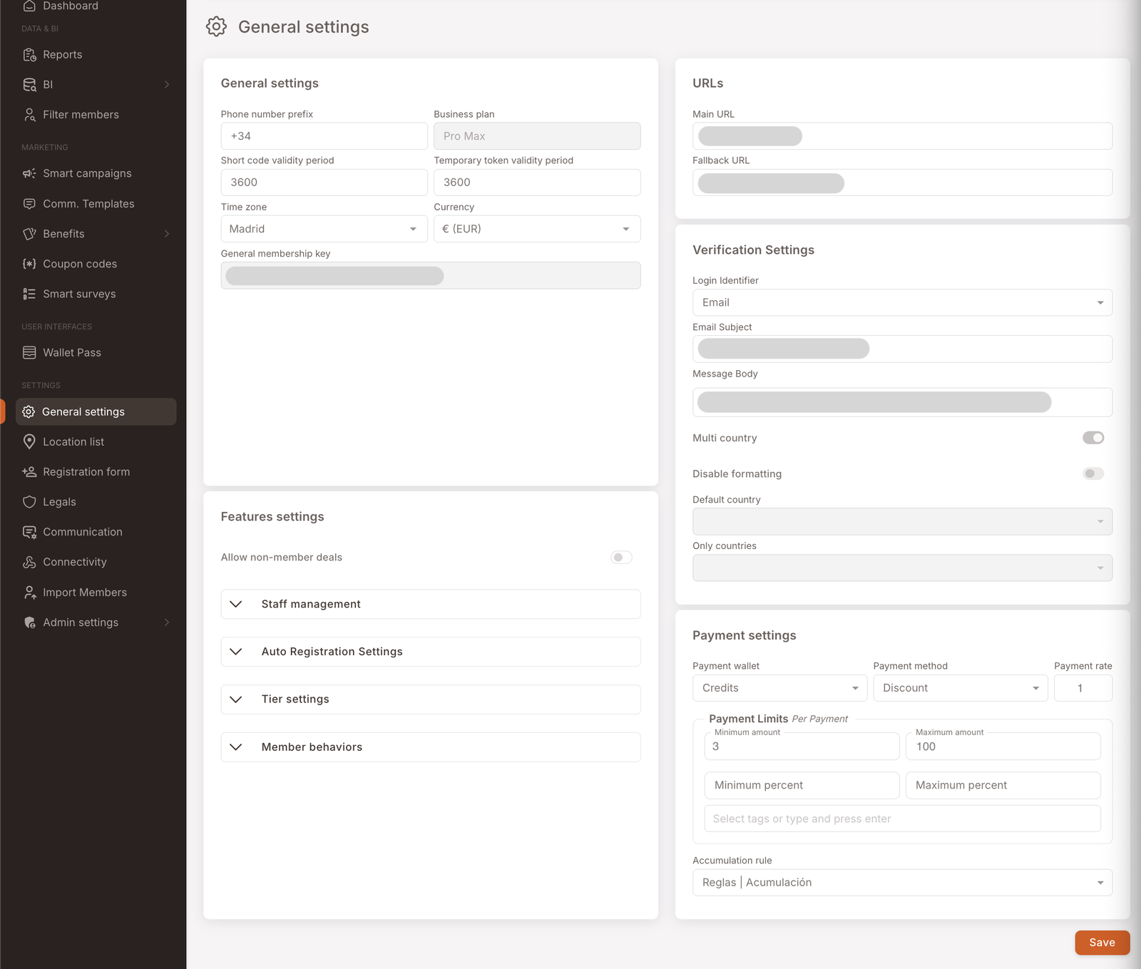 La página de Configuración general en el panel de gestión. Cinco tarjetas visibles: Configuración general (Prefijo del número de teléfono +34, Plan de negocio, Período de validez del código corto 3600, Período de validez del token temporal 3600, Zona horaria Madrid, Moneda € (EUR), Clave general de membresía); Configuración de funciones (interruptor Permitir ofertas para no-miembros, cuatro acordeones plegables: Gestión de personal, Configuración de auto-registro, Configuración de niveles, Comportamientos del miembro); URLs (URL principal, URL de respaldo); Configuración de verificación (Identificador de inicio de sesión Email, Asunto del email, Cuerpo del mensaje, interruptor Multipaís, interruptor Desactivar formato, País por defecto, Solo países); Configuración de pagos (Cartera de pago Créditos, Método de pago Descuento, Tasa de pago 1, Límites de pago por pago con Importe mín/máx y porcentaje, campo Seleccionar etiquetas, Regla de acumulación). Botón Guardar abajo a la derecha.